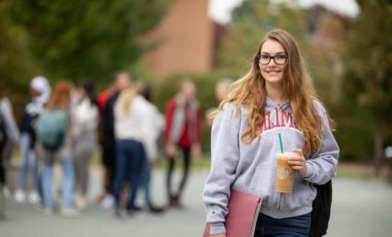 A new Hamline student smiling outside and other students in the background