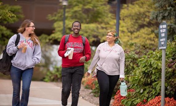 Three Hamline students walking 和 talking outside on campus in the fall