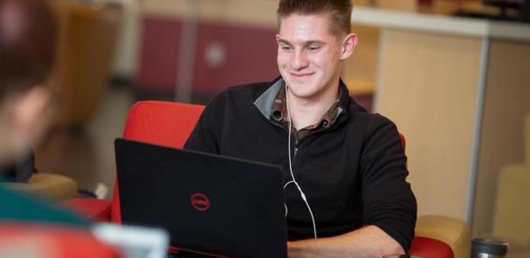 A Hamline student sitting with a laptop on their lap, smiling and typing